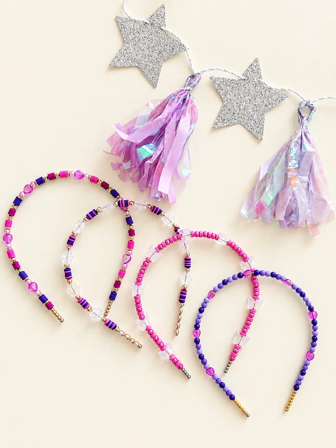 Four purple and magenta beaded headbands with heart and butterfly beads beneath a silver star garland with iridescent tassels.